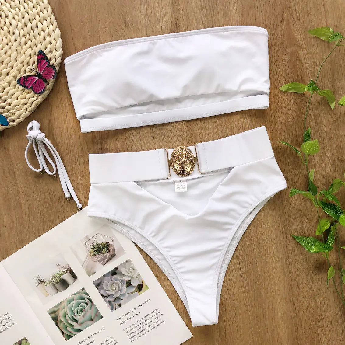 White bikini set flat lay: strapless bandeau top and high-waisted bottoms with gold clasp