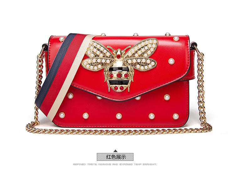 Red flap handbag with rhinestone bee clasp, pearl studs, striped strap, and gold chain.