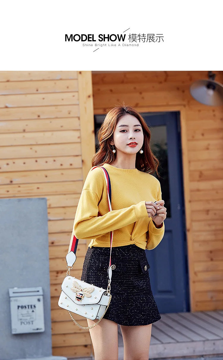 White butterfly detail crossbody bag worn with striped strap and gold chain