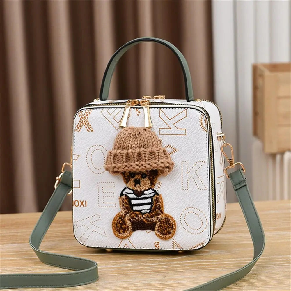 White patterned crossbody bag with teddy bear patch and knit hat, green shoulder strap