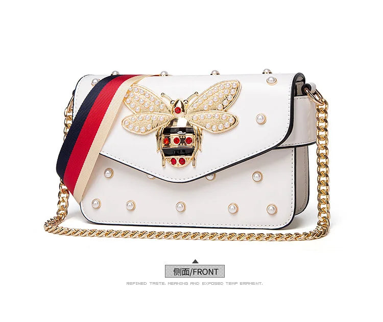 White flap handbag with rhinestone bee clasp, pearl studs, striped strap, gold chain.