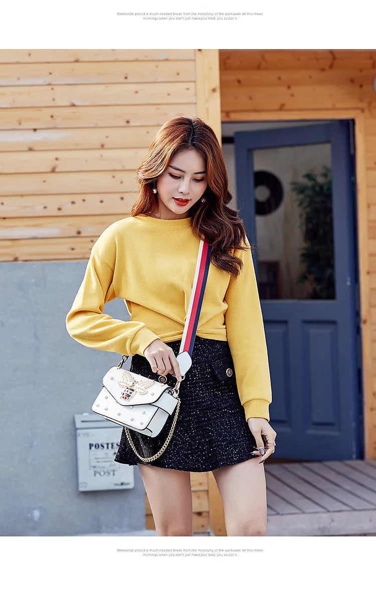 White studded crossbody bag with butterfly clasp worn on a gold chain