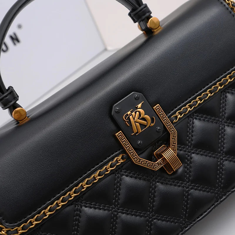 Black handbag close-up of gold emblem clasp and gold chain trim over quilted fabric