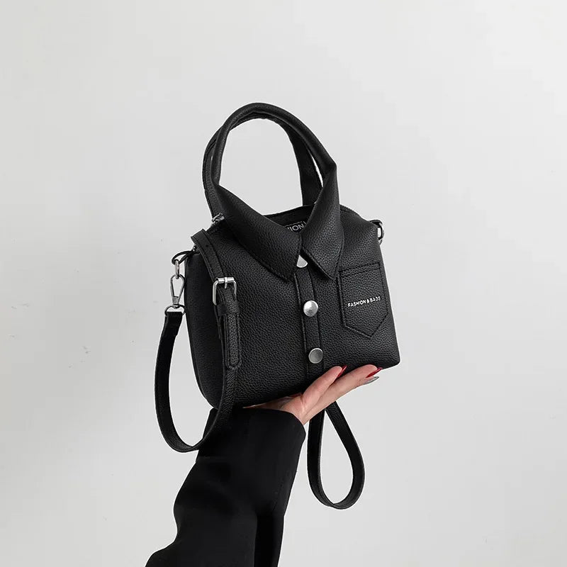 Black faux-leather handbag with top handle, wrist strap, front pocket and metal snap