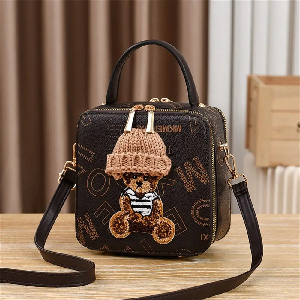 Black mini crossbody bag with gold-tone zipper and teddy applique with crochet hat topper