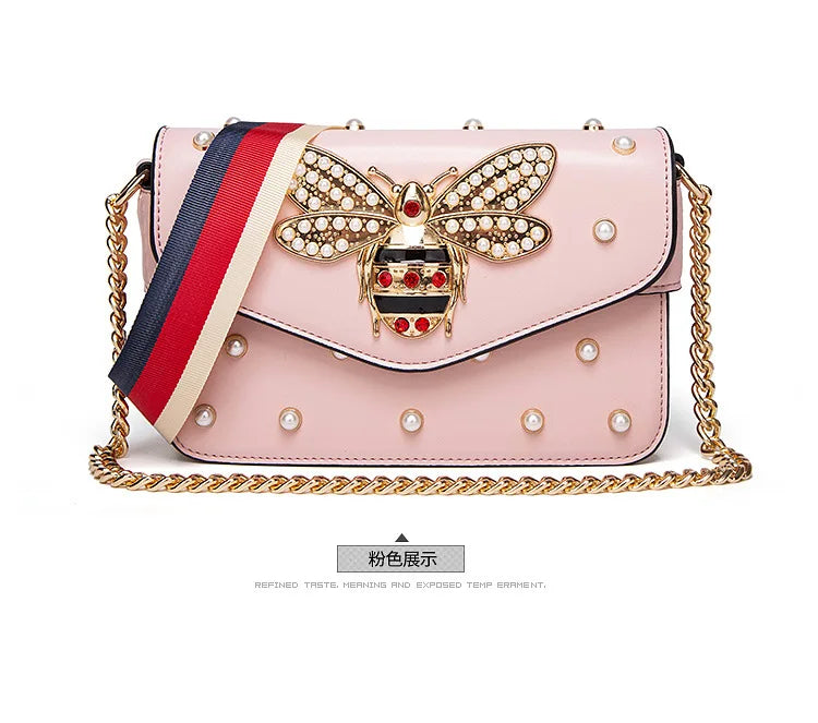 Pink flap handbag with rhinestone bee clasp, pearl studs, striped strap, and gold chain.