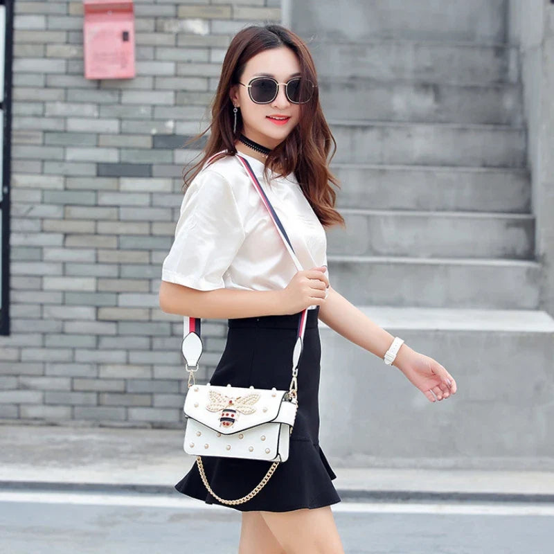 White bee bow crossbody bag with gold chain and pearl studs, worn with strap