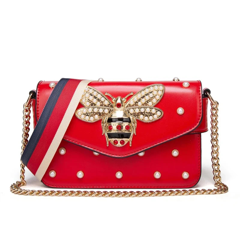 Red bee-accent flap crossbody bag with pearl studs, striped strap, and gold chain