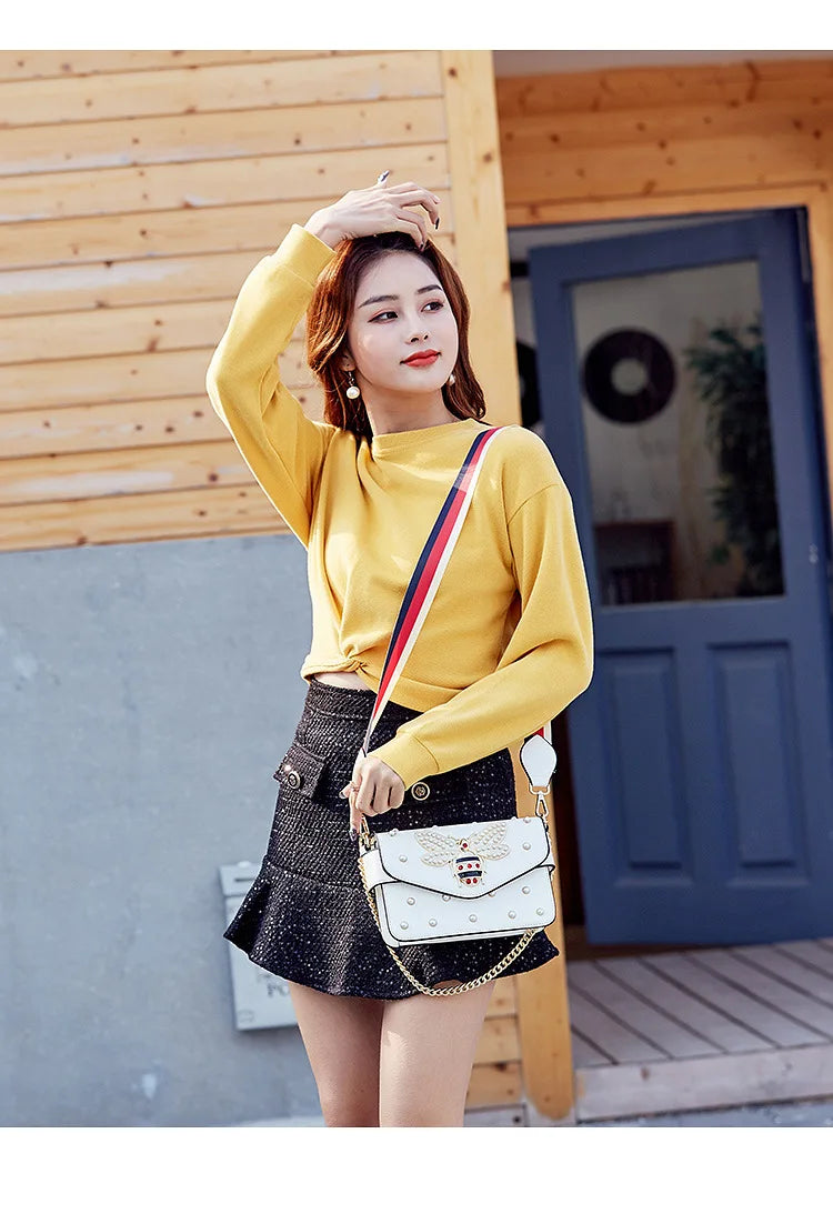 White studded crossbody bag with butterfly clasp worn at the hip
