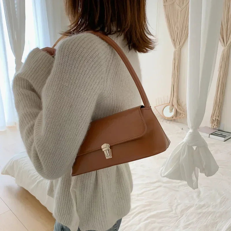 Small tan shoulder bag with curved handle and gold-tone front clasp