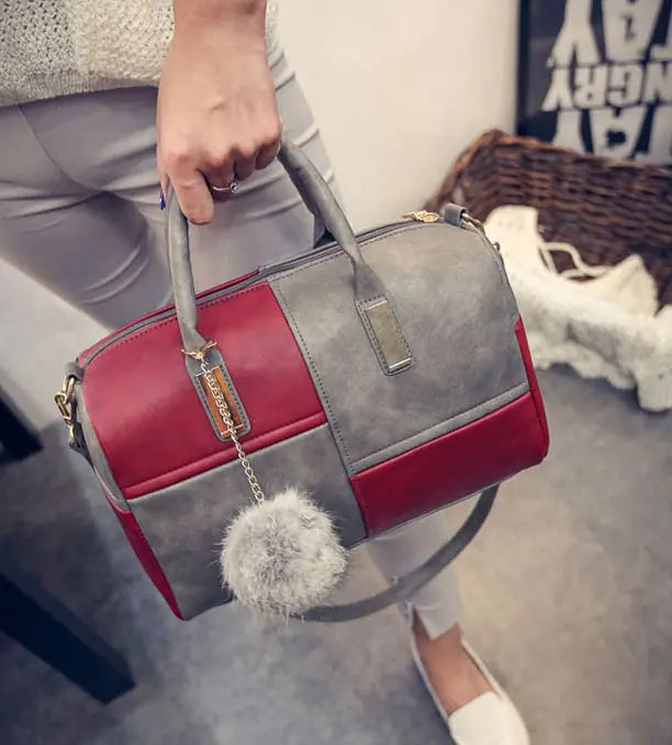 Red and gray color-block duffel bag with top handle, chain strap, and pom-pom charm