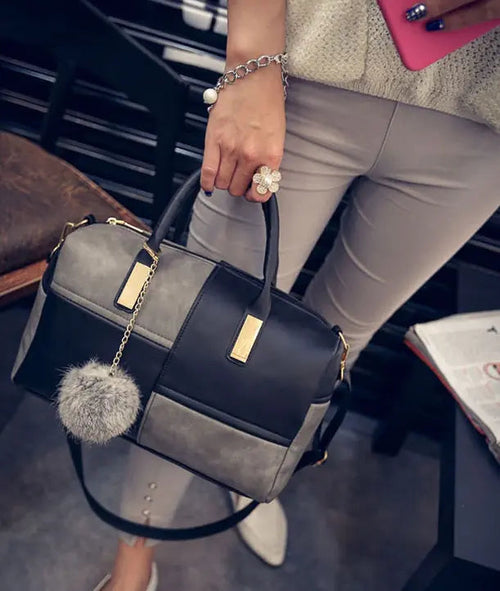 Color-block duffel bag in dark navy and gray with chain strap, top handle, pom-pom